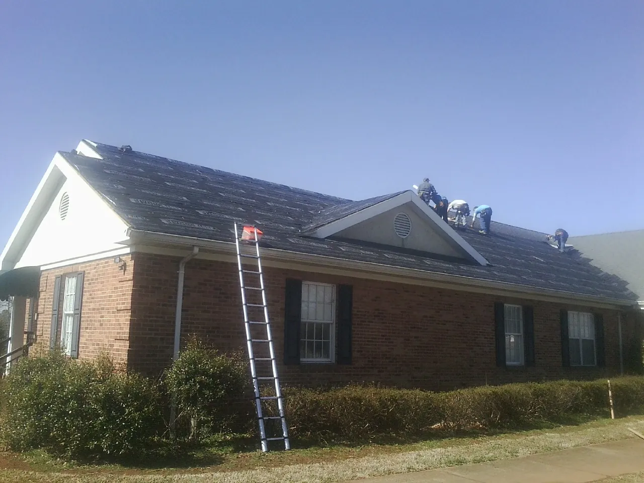 Crew tearing shingles off a brick ranch roof with a ladder set — Metal Roof Repair work by our crew in Cedar Grove