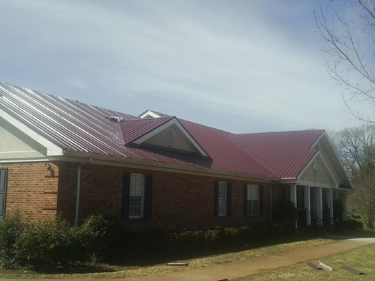 Red metal roof with gabled entries on a long brick building, from a Hail Damage Roof Repair job in Cedar Grove