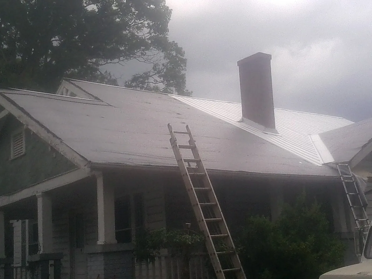 Ladders against a metal roof on an older home with a brick chimney in Cedar Grove